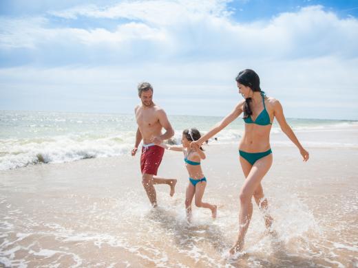 Famiglia che corre felice sulla spiaggia con il mare sullo sfondo.