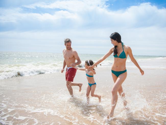 Famiglia che corre felice sulla spiaggia con il mare sullo sfondo.